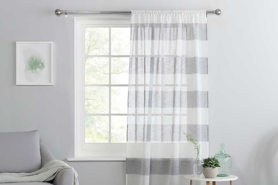A Habitat grey and white striped linen pencil pleat sheer curtain on a window.