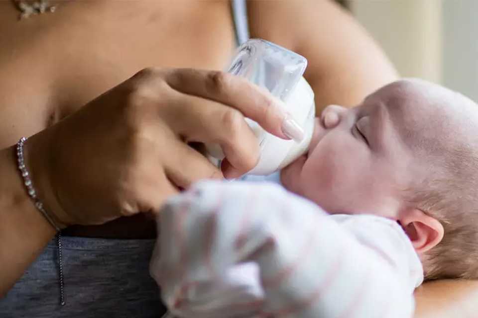A mother feeding her baby using a Tommee Tippee Breast Milk Collector bottle.