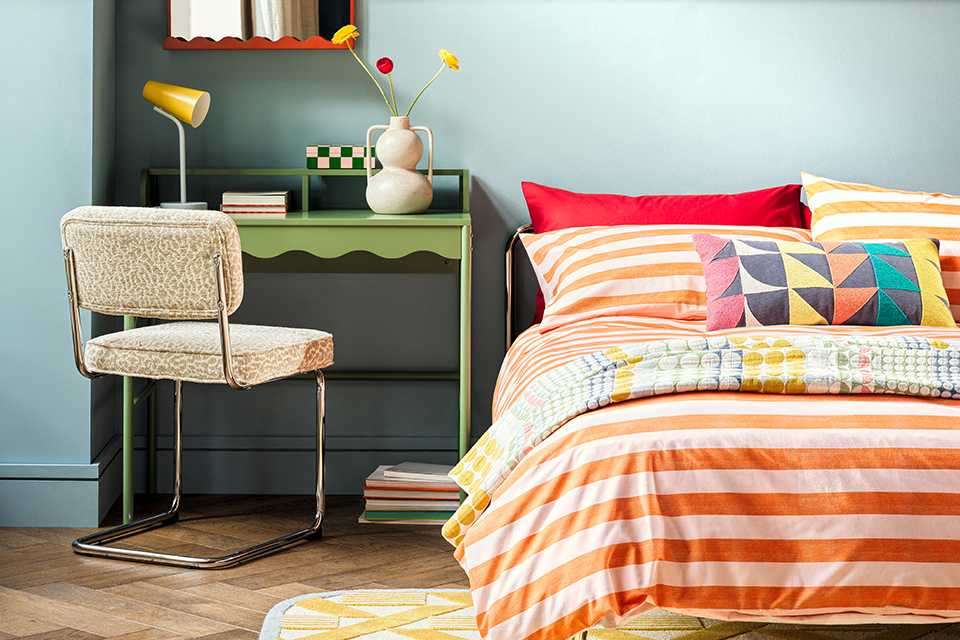 Bright bedroom with red and white stiped bedding with bold patterned cushions and green dressing table.