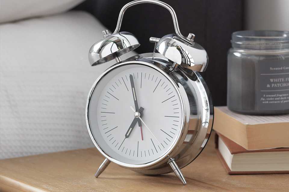 A silver Constant Twin Bell alarm clock on a bedside table.