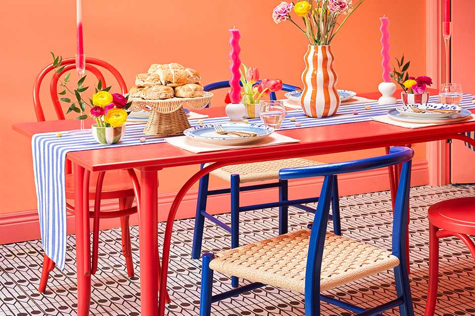 A red colour dining table decorated for Easter with candles, vase, a cake stand, dinnerware, and a table runner.