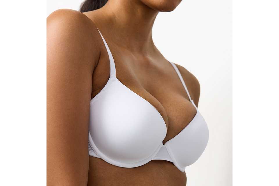 A woman wearing a white bra, checking that the underwire doesn't hurt.