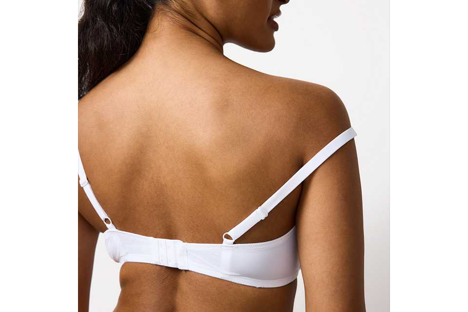 A woman wearing a white bra checking that her straps aren't falling off.