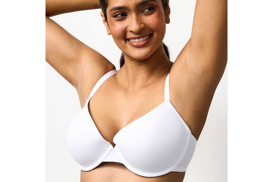 A woman earing a white bra lifting her arms up into the air.
