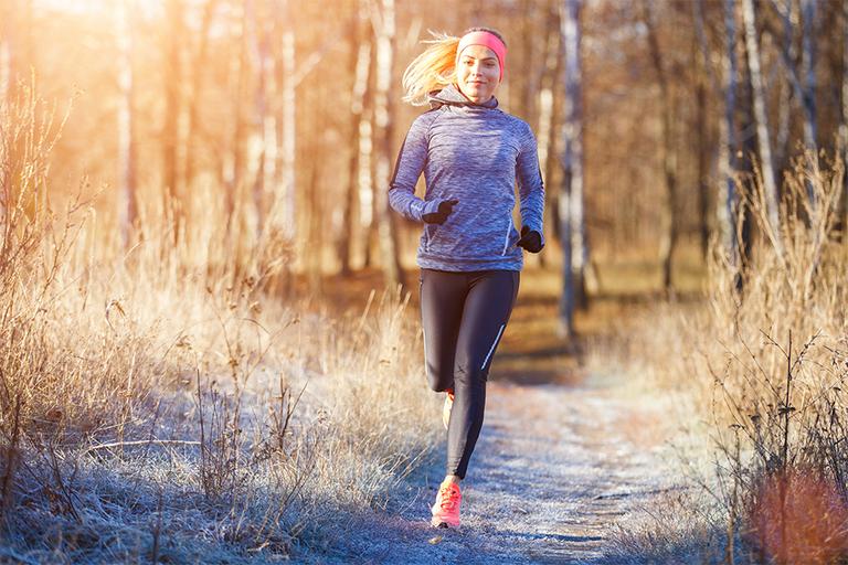 Woman running outside in cold weather with a long sleeve top, leggings and running gloves on.