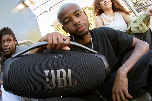 Three people sitting on stairs, with one man holding a JBL Boombox 3 speaker at the front.