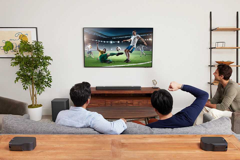 Three men sitting in living room watching football on TV, with JBL Bar 800 surround speakers.