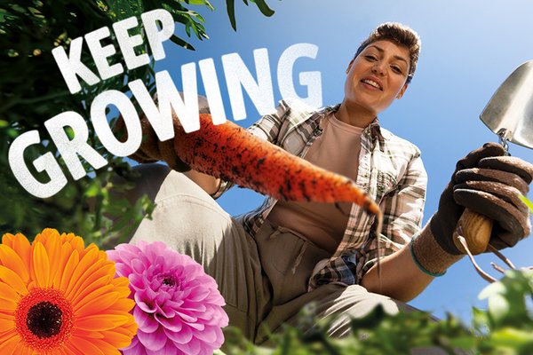 A woman smiling and preparing a garden bed for carrots with a hand trowel on a bright day.