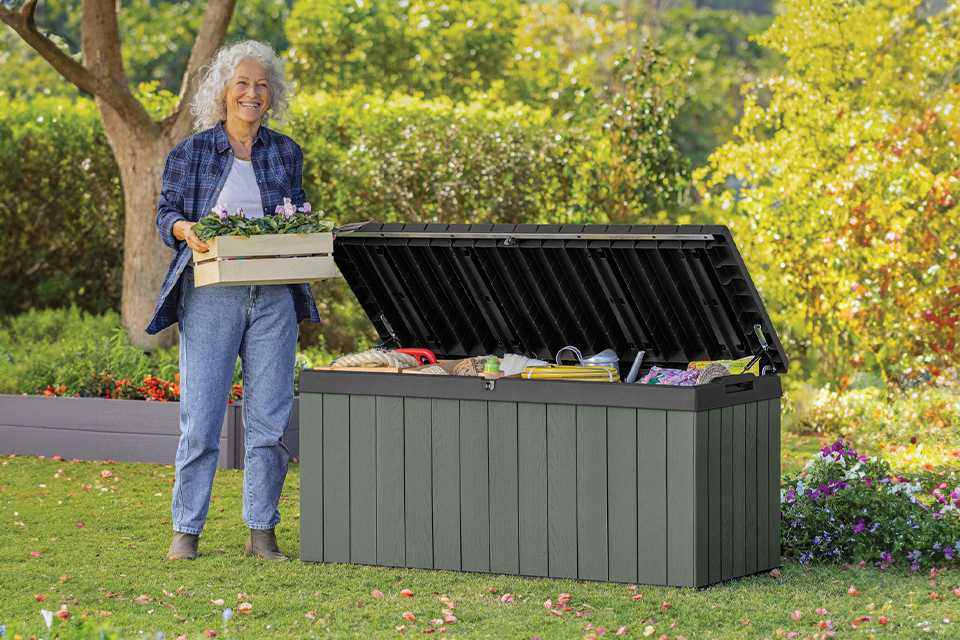 A woman standing next to a Keter Darwin 454L Outdoor Garden Storage Box in green colour.