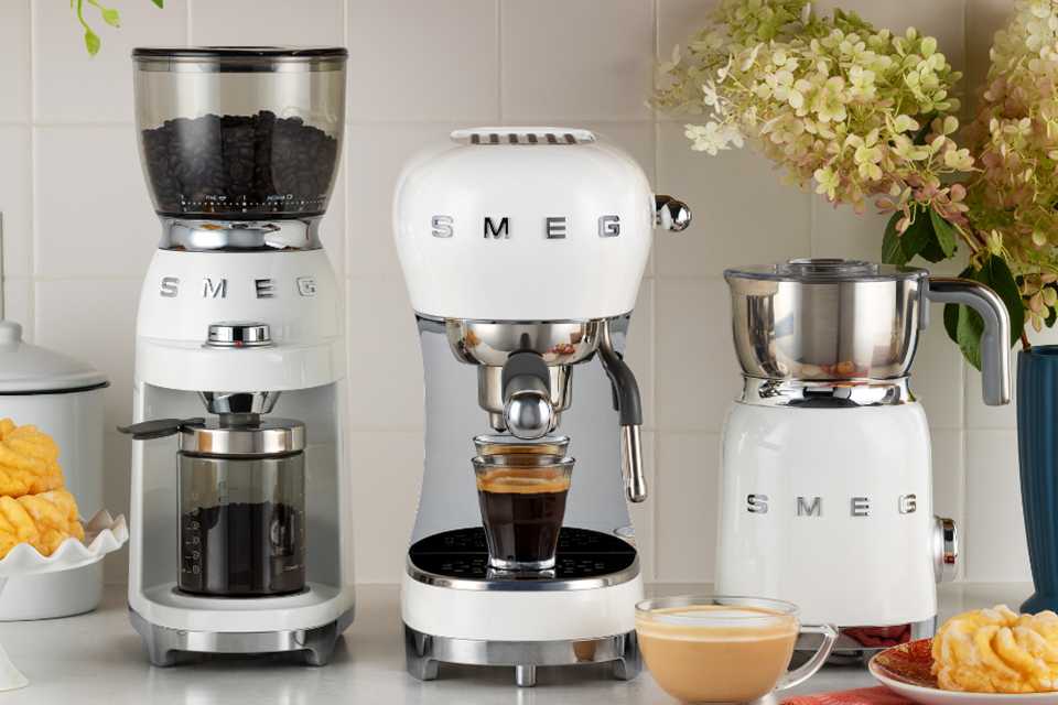 White Smeg coffee grinder, espresso machine and milk frother placed on a kitchen countertop.