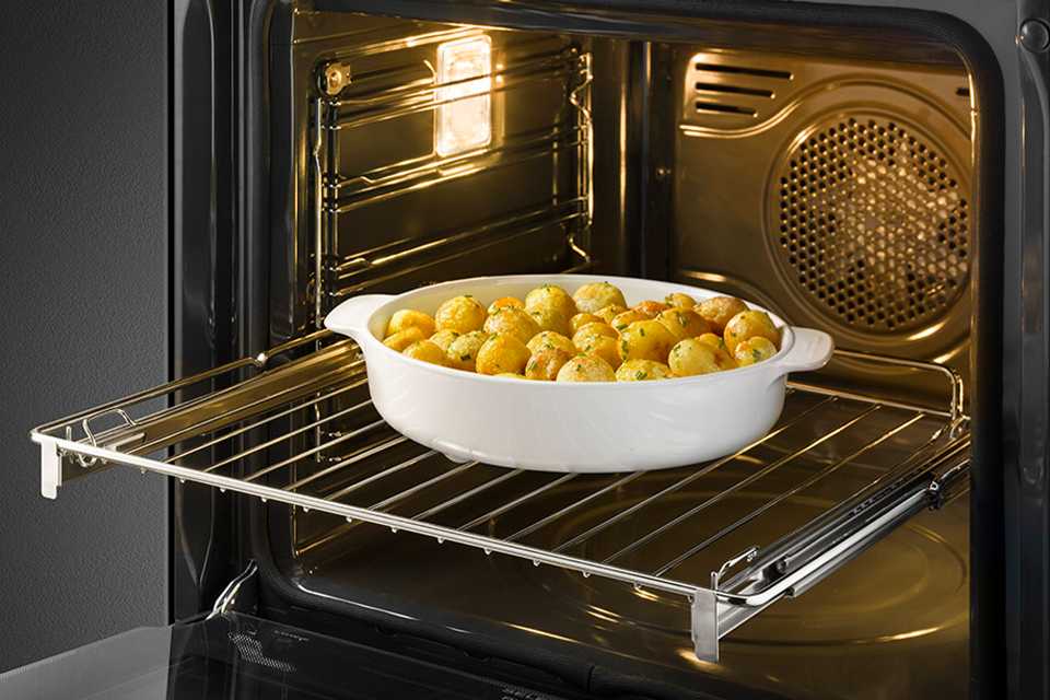 The internal view of a Smeg oven with a tray of baked potatoes in it.