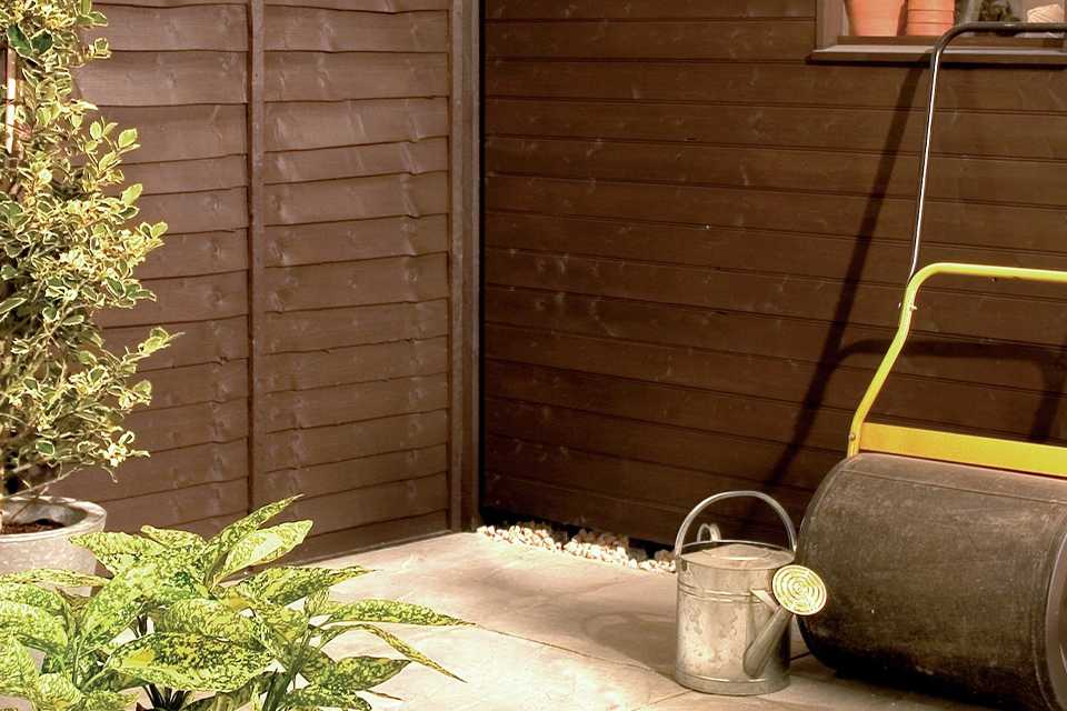 A shed and fence painted with Johnstone's shed & fence paint in dark oak.