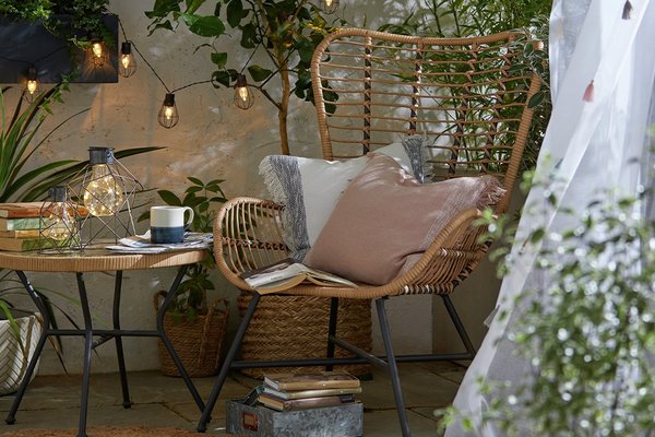 Cosy wicker garden chair and side table with warm string lights.