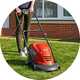 A woman using a Flymo Hover Vac 250 25cm corded Hover 1400W lawnmower to mow a lawn.