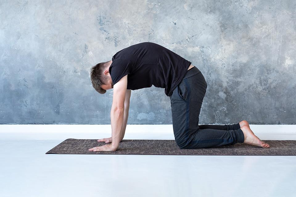 Man doing cat and cow pose on yoga mat.