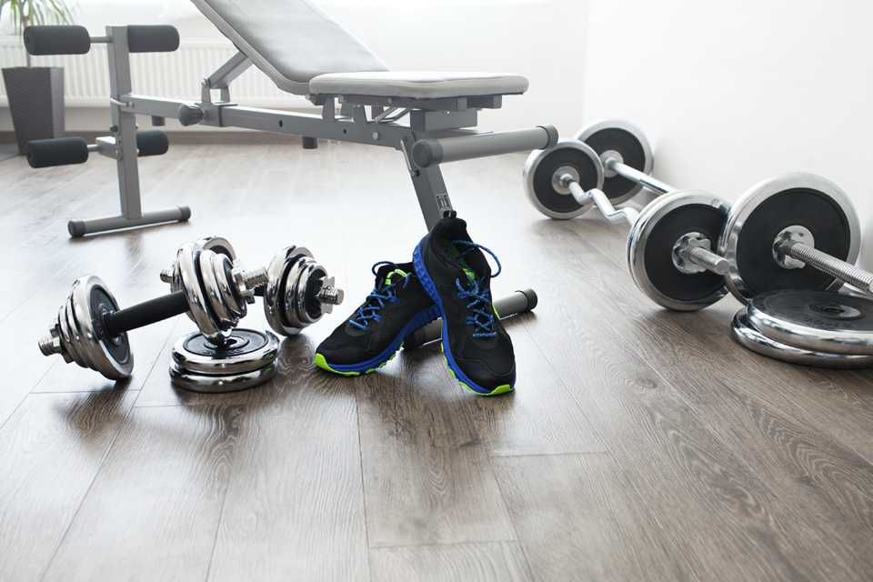 A pair of trainers and dumbbells placed next to a workout bench in a gym.