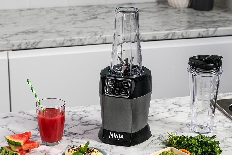 Blender surrounded by fruit and smoothies.