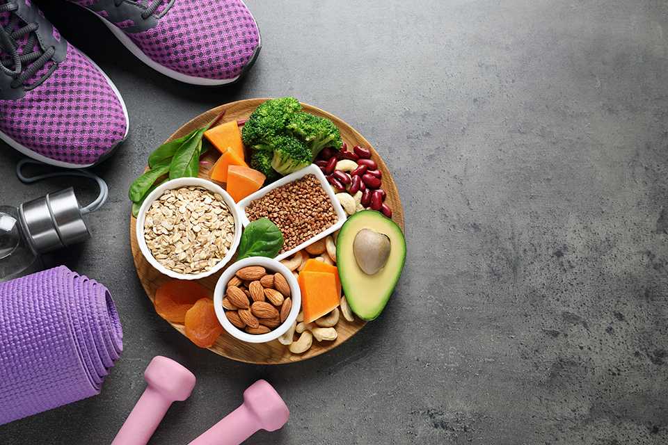 A bowl of fruits and vegetables alongside a set of dumbbells.