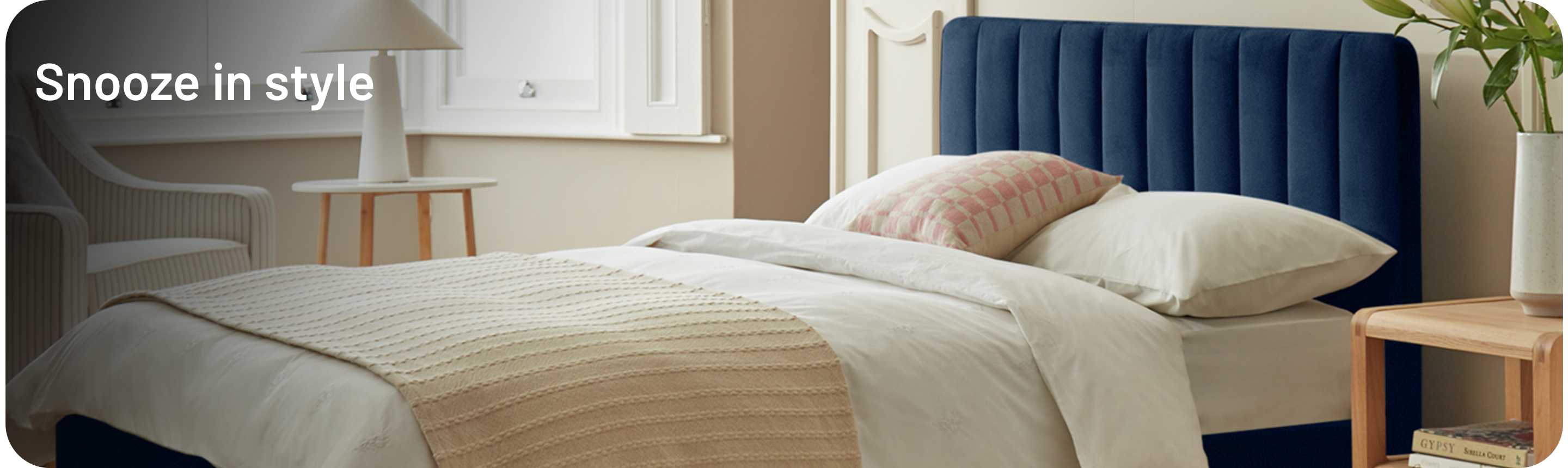 Throw, pillows and blanket neatly layered over a dark ink blue ottoman bed in a bedroom.