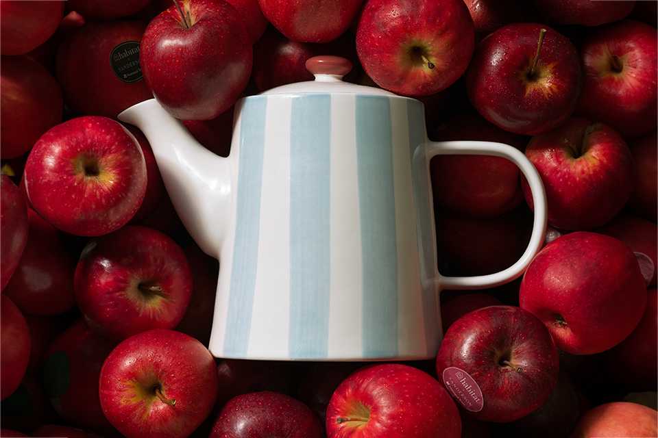 National trust blue and white striped tea pot on top of red apples.