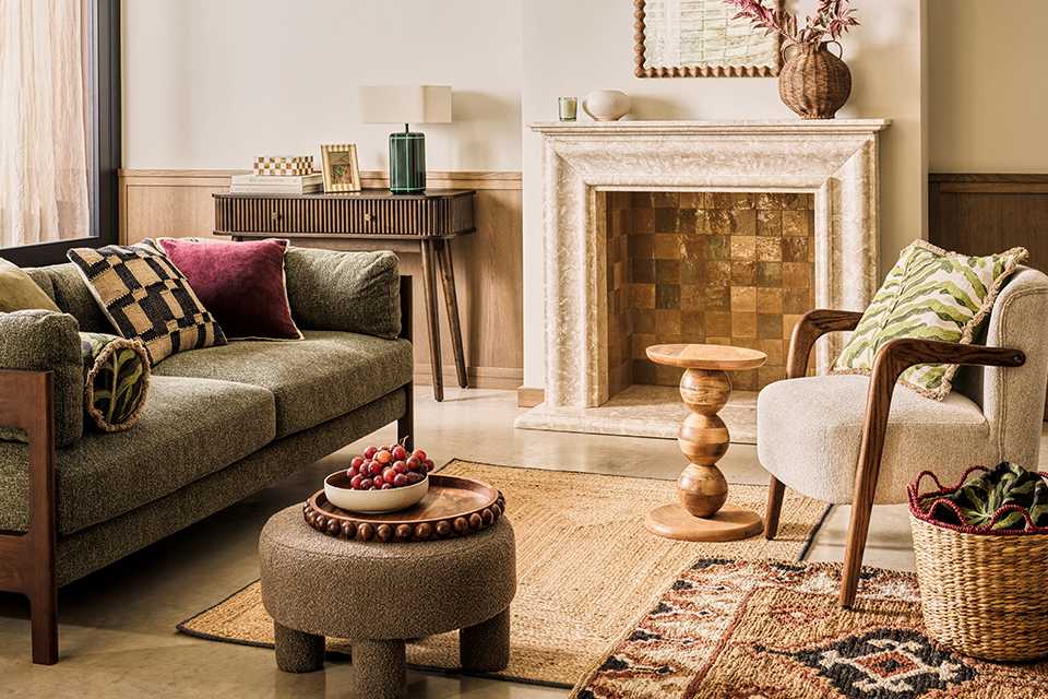 Neutral living room with light green velvet sofa with dark wooden arms and white accent chair in corner with wooden arms and touches of florals and woven basket on top of a persian rug.
