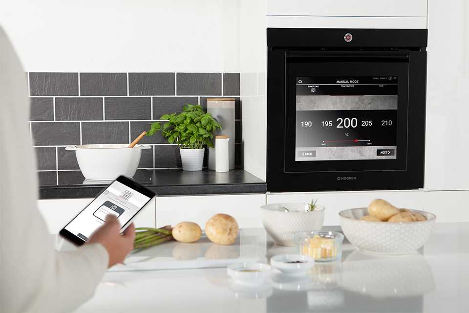 A person operating the oven with the help of mobile.