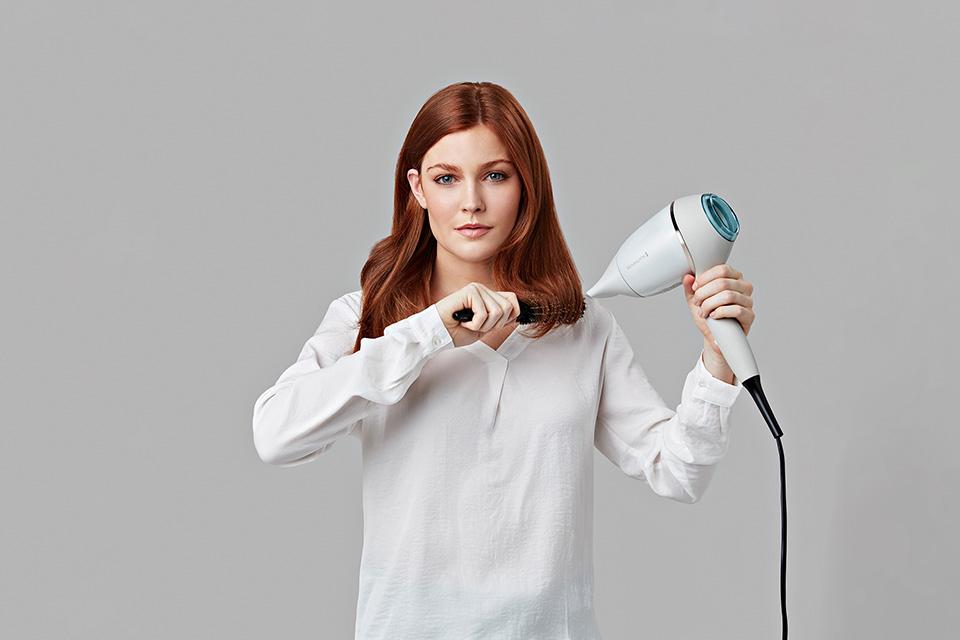 Woman blow drying her hair using a hair brush.