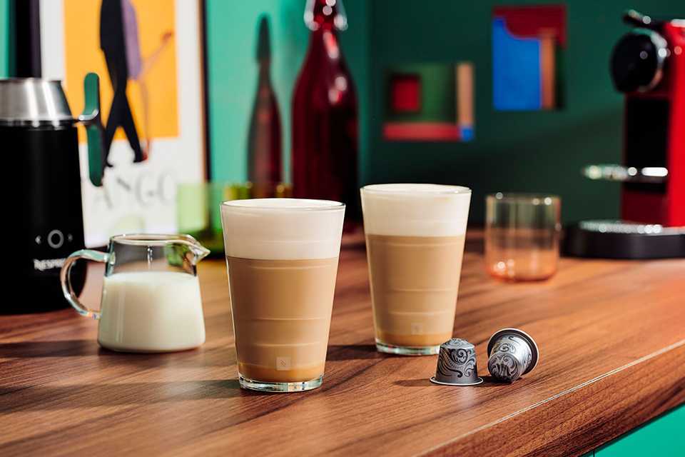 Two cups of coffee with a milk jug and Nespresso Vertuo capsules next to it.