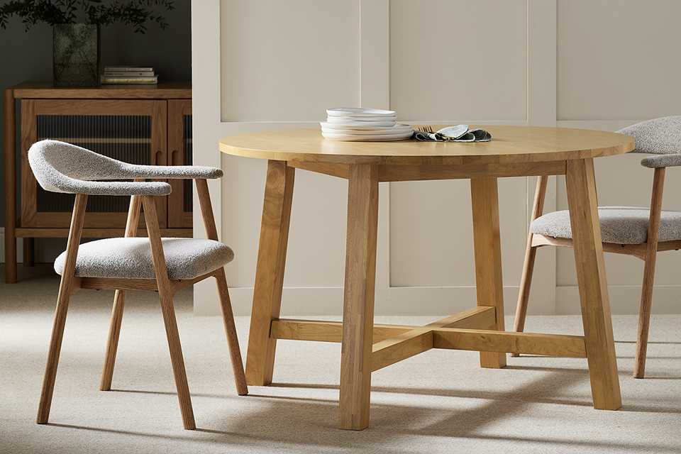 A Habitat Trieste round oak 4 seater dining table with chairs on either side of it.