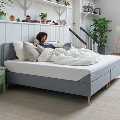 A woman sitting on a bed with a comfy mattress and duvet.