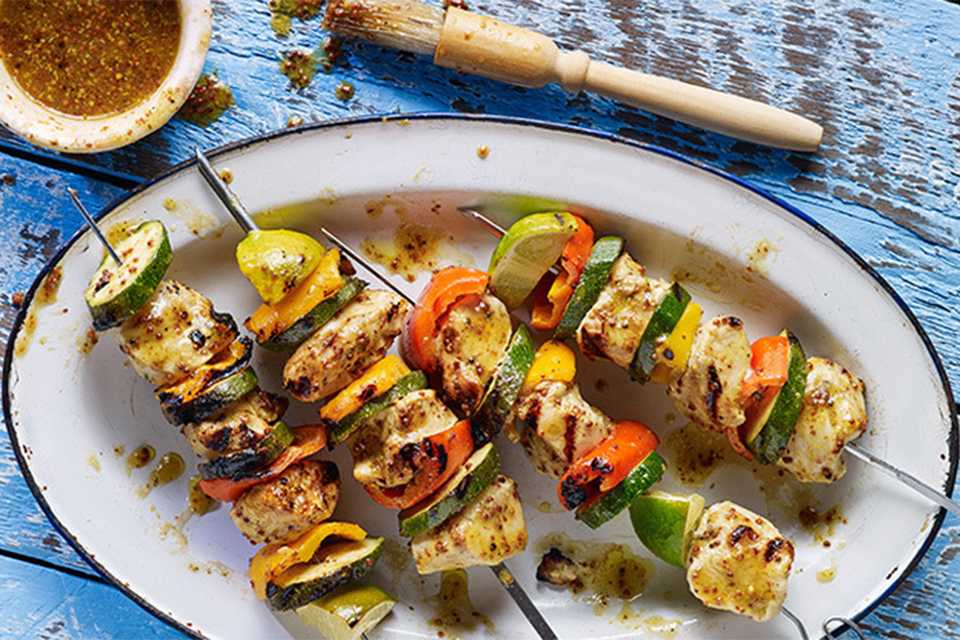 A top angle view of chicken kebabs on BBQ skewers along with bell peppers and other vegetables.