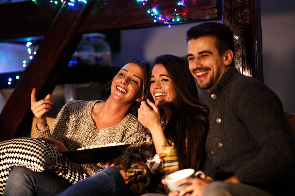 A group of housemates laughing at a film with a bowl of popcorn.