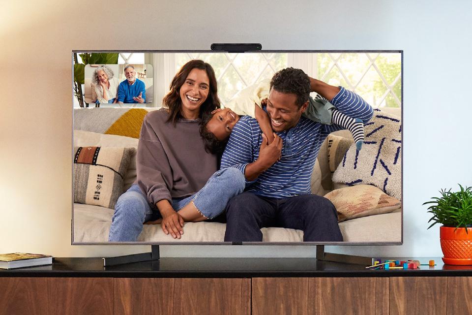 A smiling family are displayed on a large screen. They're talking to an older couple, shown in preview at the top left of the screen.