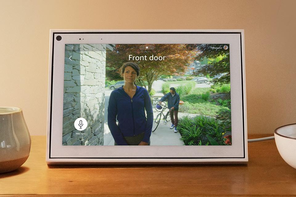 A Portal screen shows the view from a front door, with a woman standing outside and a man wheeling a bicycle coming up the path behind.