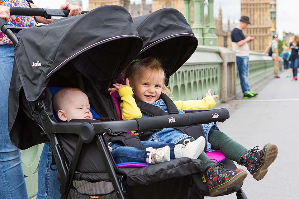 A mother pushing her two children in the Joie aire™ twin stroller.