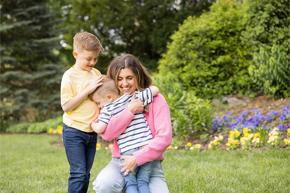 A mother playing with her two children in the garden with smiles all around.