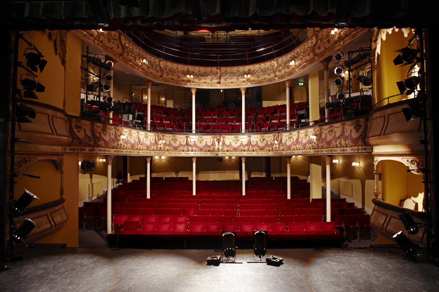 View of an empty theatre with red seats and balcony all hand.