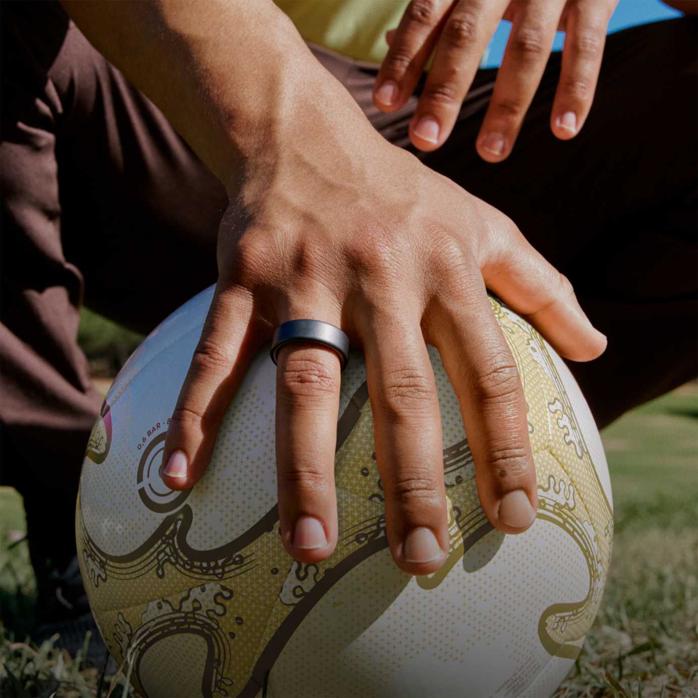 Space grey colour Oura Ring 4 on a hand resting on top of a football