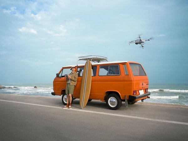 A man using a DJI Lito X1 Fly More 33MP camera drone outside his van near a seashore.