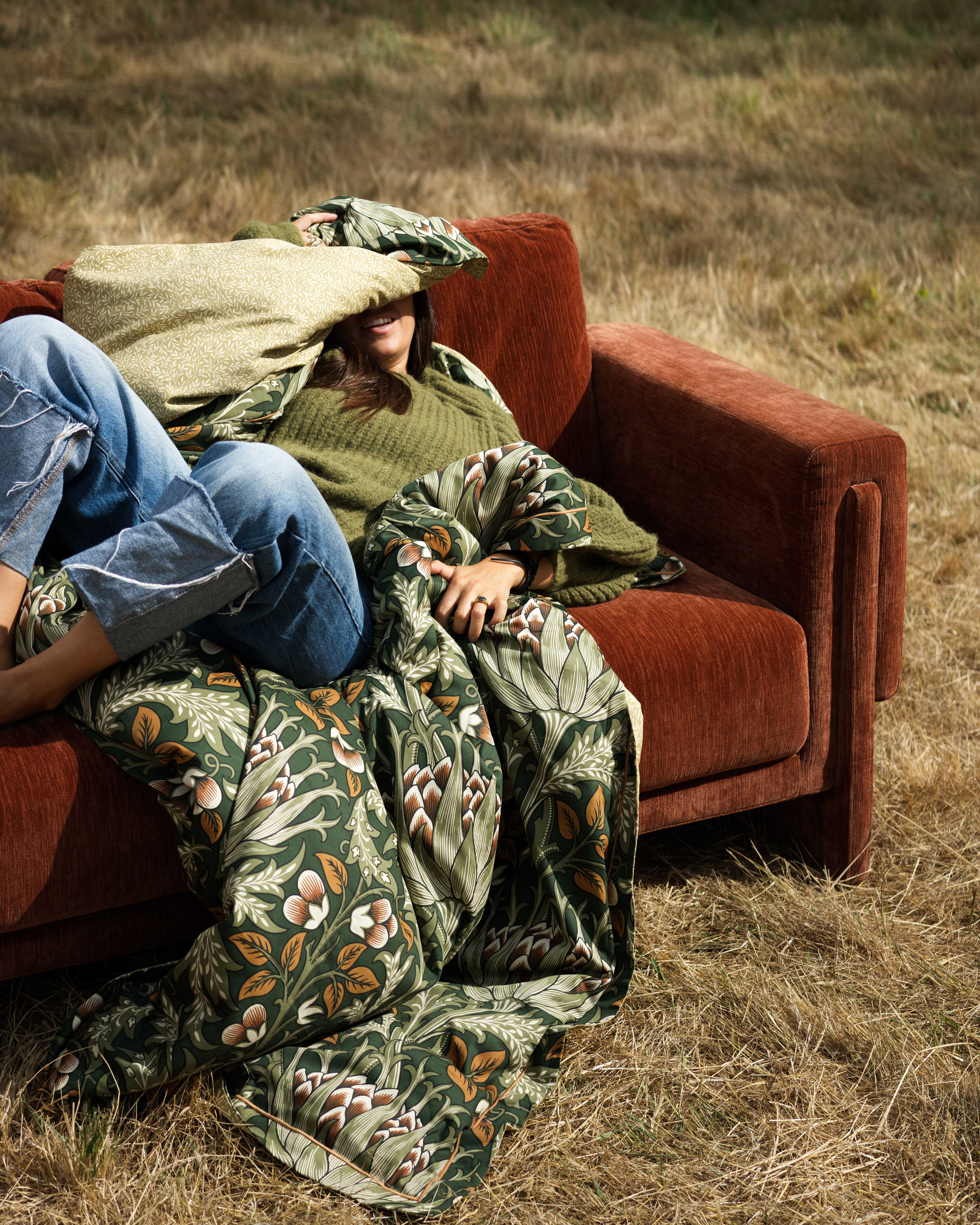 person on sofa in field in orange colour with blankets and cushions