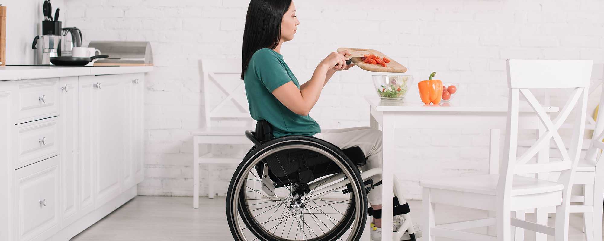 A woman in a wheelchair chopping vegetables in her kitchen.