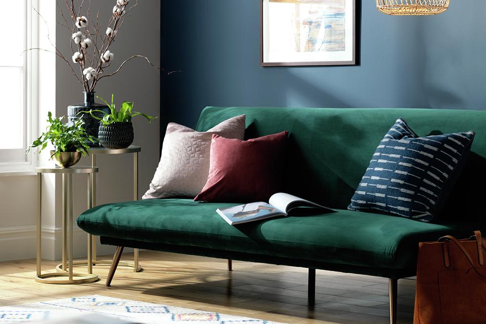 A teal coloured Habitat velvet sofa bed placed in a blue room.