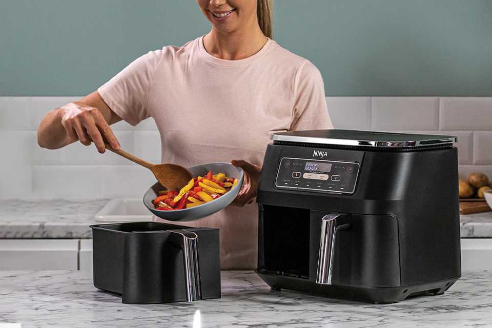 A woman cooking vegetables in a Ninja air fryer and dehydrator.