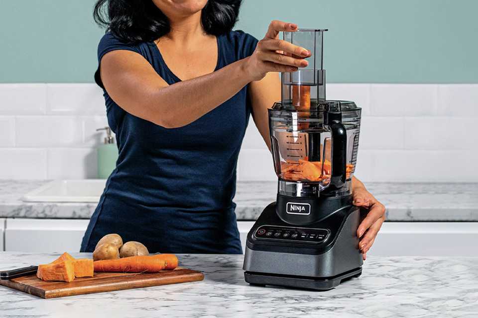 A woman slicing vegetables in a Ninja food processor.