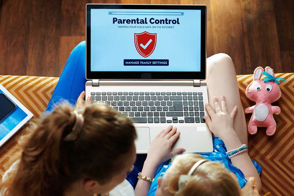 A woman activating parental control on a laptop with her kid sitting next to her.