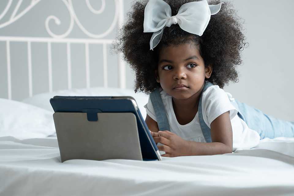 A kid lounging on her bed with a laptop open in front of her.