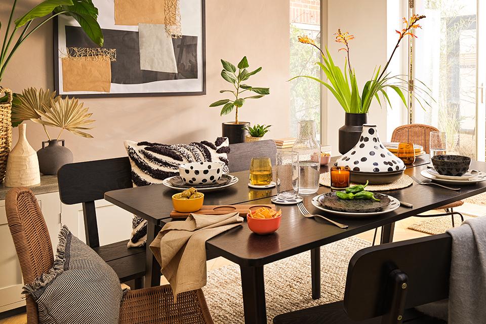 A dining room with a black dining table displaying glassware, tableware, vase and a tagine cooking pot.