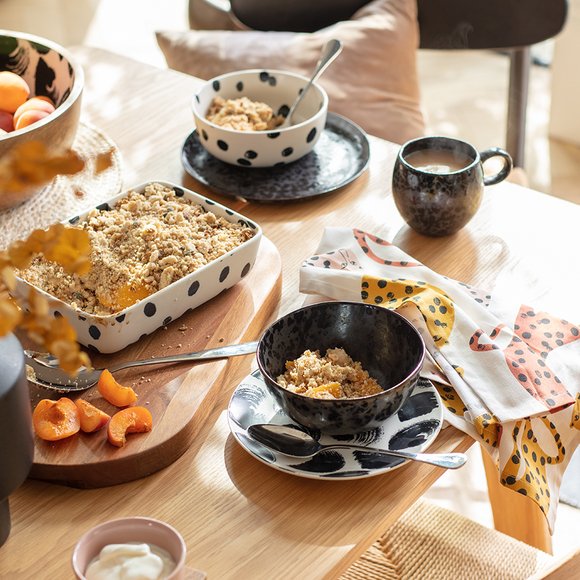 A dining table displaying black and white polka dot print serveware and dinnerware with an animal print tea towel.