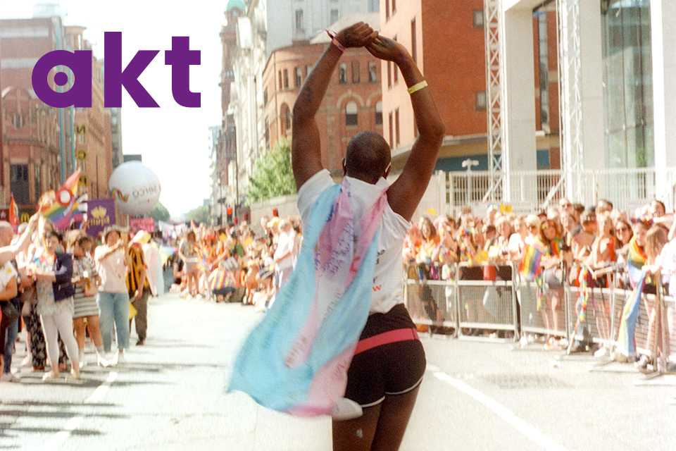 A person walking in a parade wearing a pink and blue transgender pride flag.