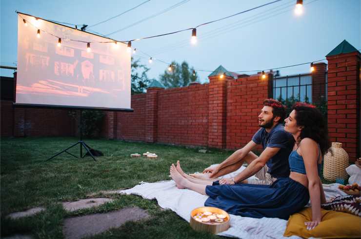 a couple sit in the garden, watching a film on a projector and screen